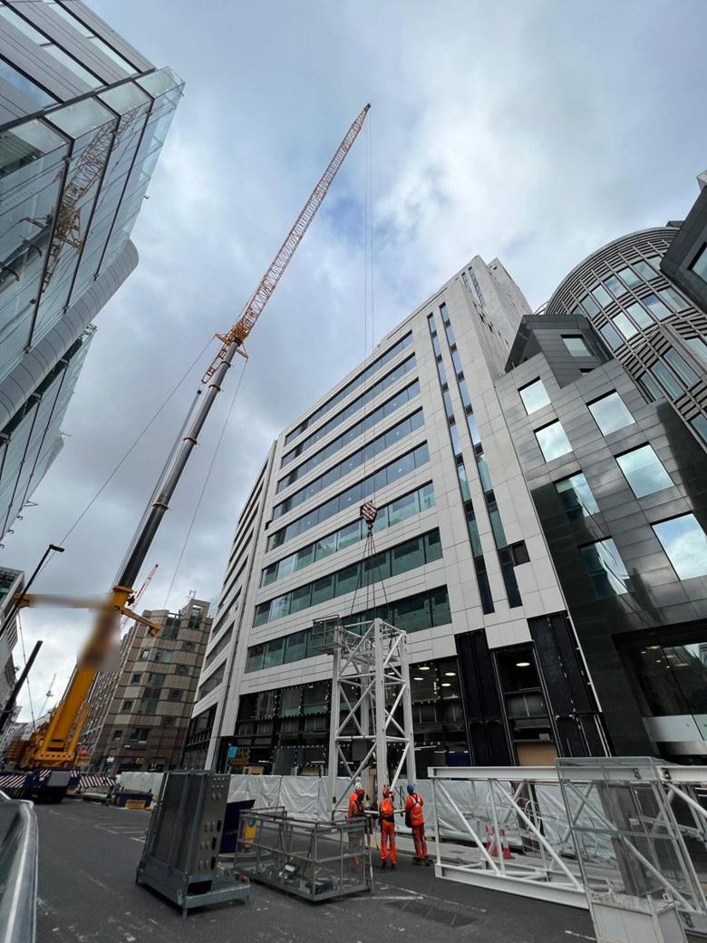 Mobile crane lifting a tower crane mast section into place in a City street