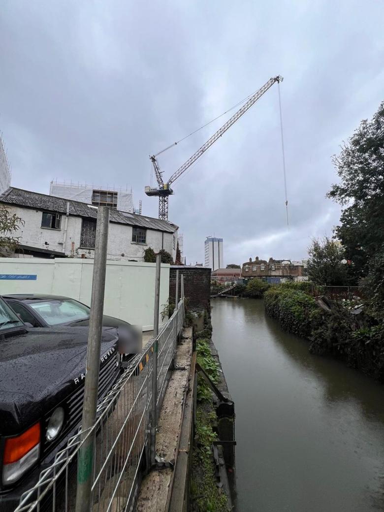 Luffing-jib tower crane working over a river next to a live site