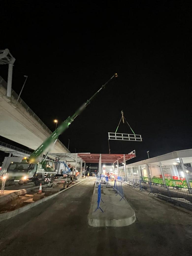 Mobile crane lifting a steel frame at night beside a flyover